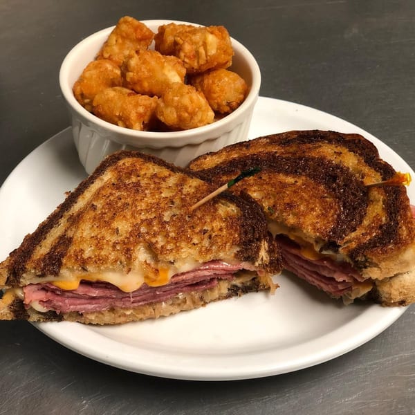 Hardy's catering offers a grilled Reuben sandwich with melted cheese and corned beef, served with tater tots.