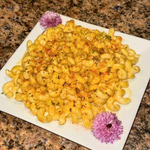 Hardy's catering mac and cheese, garnished with spices and two purple flowers on a white plate.