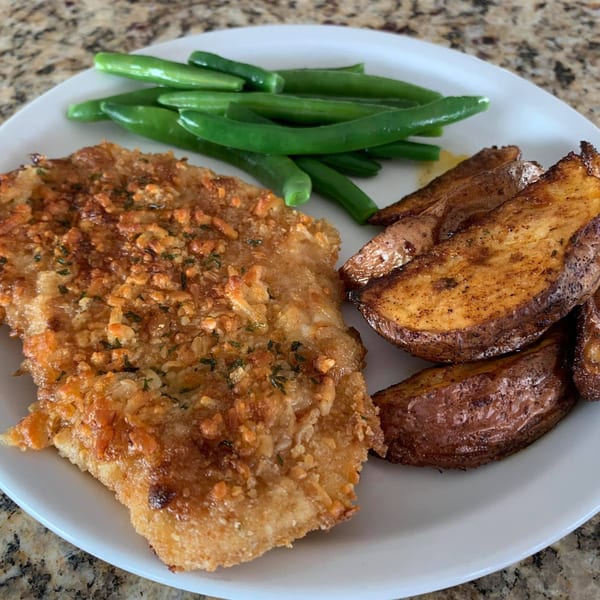 Crispy baked chicken with roasted potato wedges and green beans on a white plate.